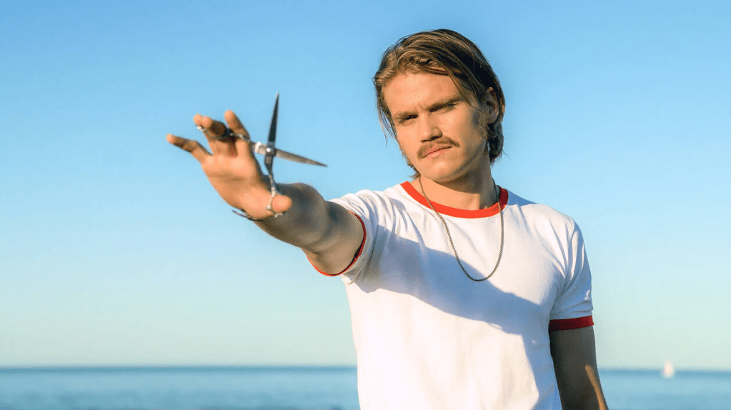 Un Albert joven sostiene unas tijeras, de espalda al mar en la serie francesa 'Las mariposas negras' de Netflix