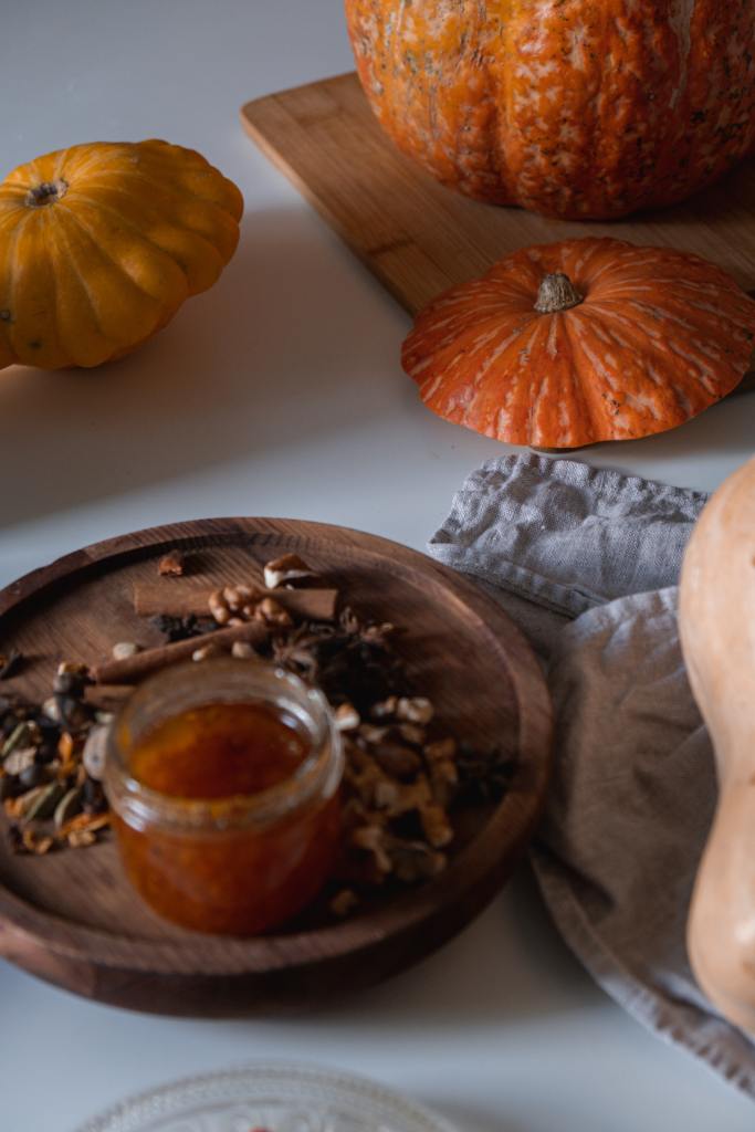 Frasco de mermelada de calabaza, sobre platón de madera. Se ven pequeñas partes de distintas calabazas alrededor. 